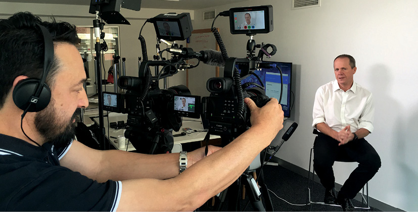 A video camera operator controlling a series of cameras and wearing headphones films Chief Executive Officer Gavin Slater.